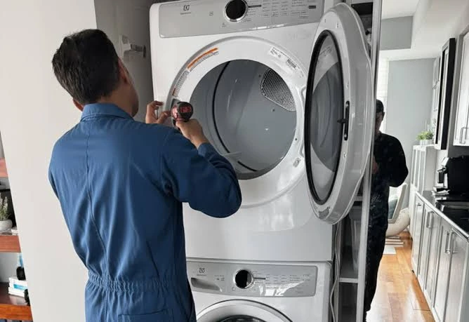 Technician repairing a front-loading dryer in a stacked laundry setup